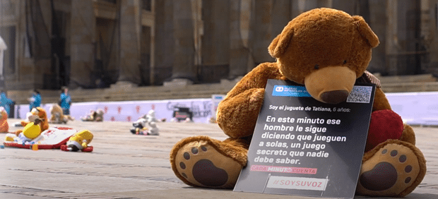 En brun bamse sitter på et fortau og holder en plakat. Foto: SOS-barnebyer Colombia