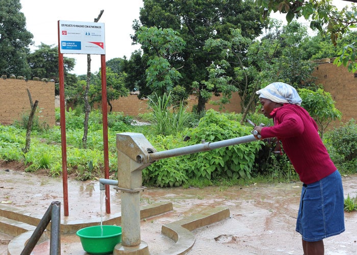 Isabel med hvitt skaut, rød skjorte og blått skjørt pumper vann i en stor balje. Foto: SOS-barnebyer