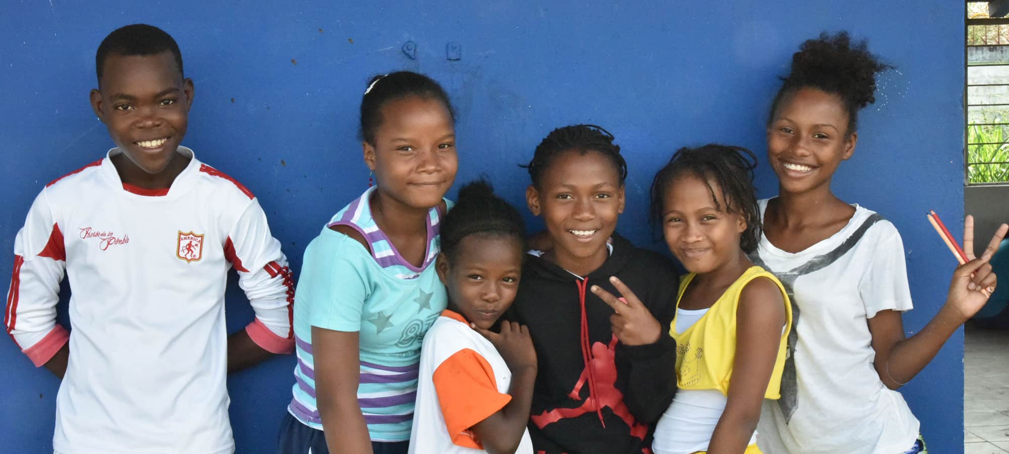 Fem jenter fra Colombia står tett sammen og smiler. Bak dem er det en blå vegg. Foto: Giti Carli Moen