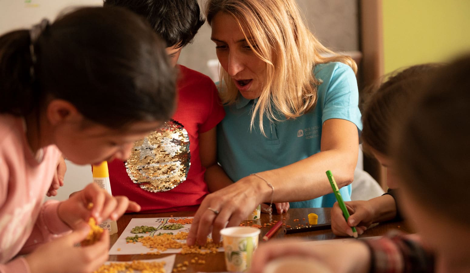 Sosialarbeider fra SOS-barnebyer med lyst hår og blå t-skjorte med logo, spiller spill med tre barn. Foto: Katerina Ilievska