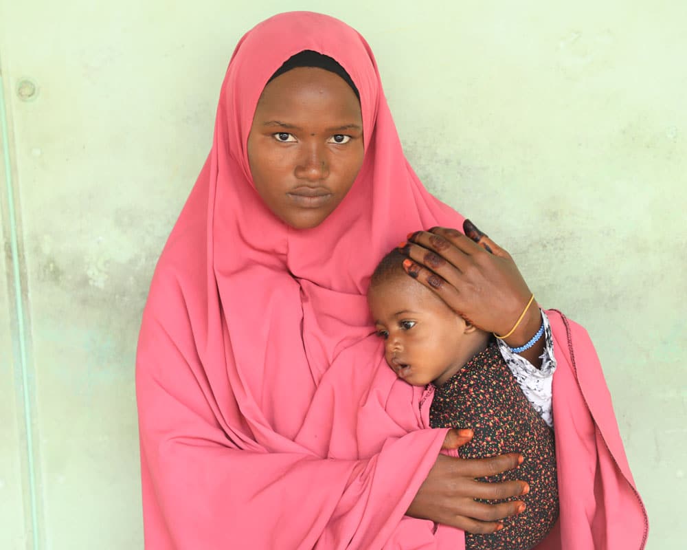 Ung alvorlig mor fra Somalia i rosa hijab holder den lille babyen, sin tett inntil seg. Foto: Sunshine Media
