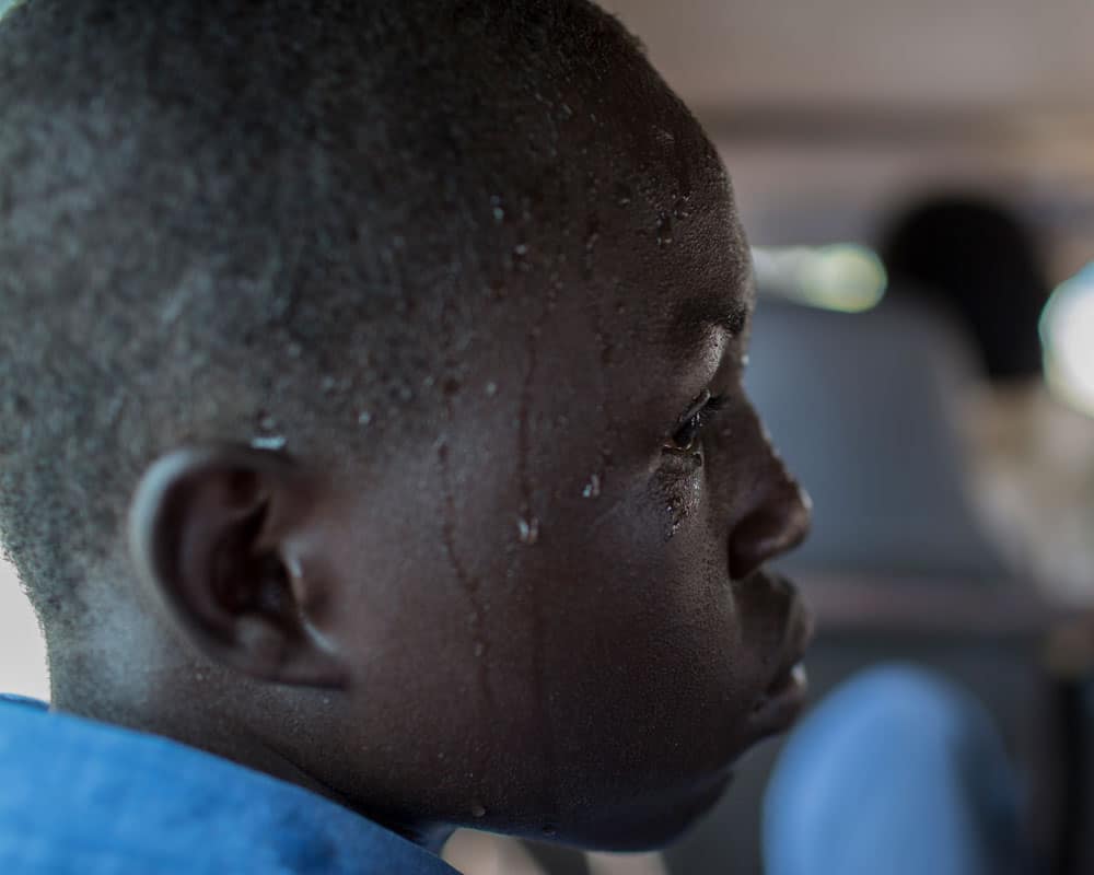 Portrett av gutt fra Sudan i profil. Han er alvorlig og svettedråper rennende nedover kinnet. Foto: Conor Ashleigh