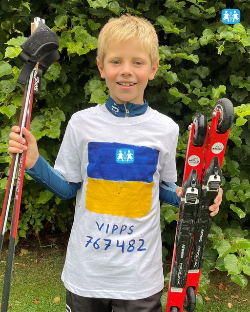 Magnus har kort lyst hår, hvit t-skjorte der det er malt ukrainas flagg og Vippsnr. 767482. Han holder rulleski og staver i hendene. Foto: Privat