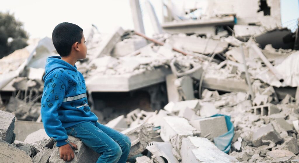 En liten gutt sitter og ser utover ruiner i Gaza etter bombing, 2023. Fotograf: Salah Hosny