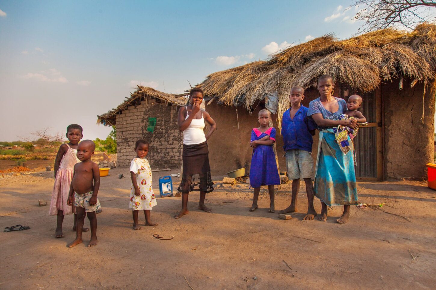 Twongo står uten for huset sitt som er laget av leire og strå, sammen med de syv barna sine. Foto: Georg Kurian