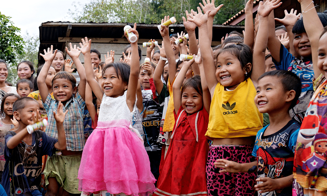 En gjeng med smilende barn i Laos som strekker hendene i været. Foto: Agnete Schlichtkrull
