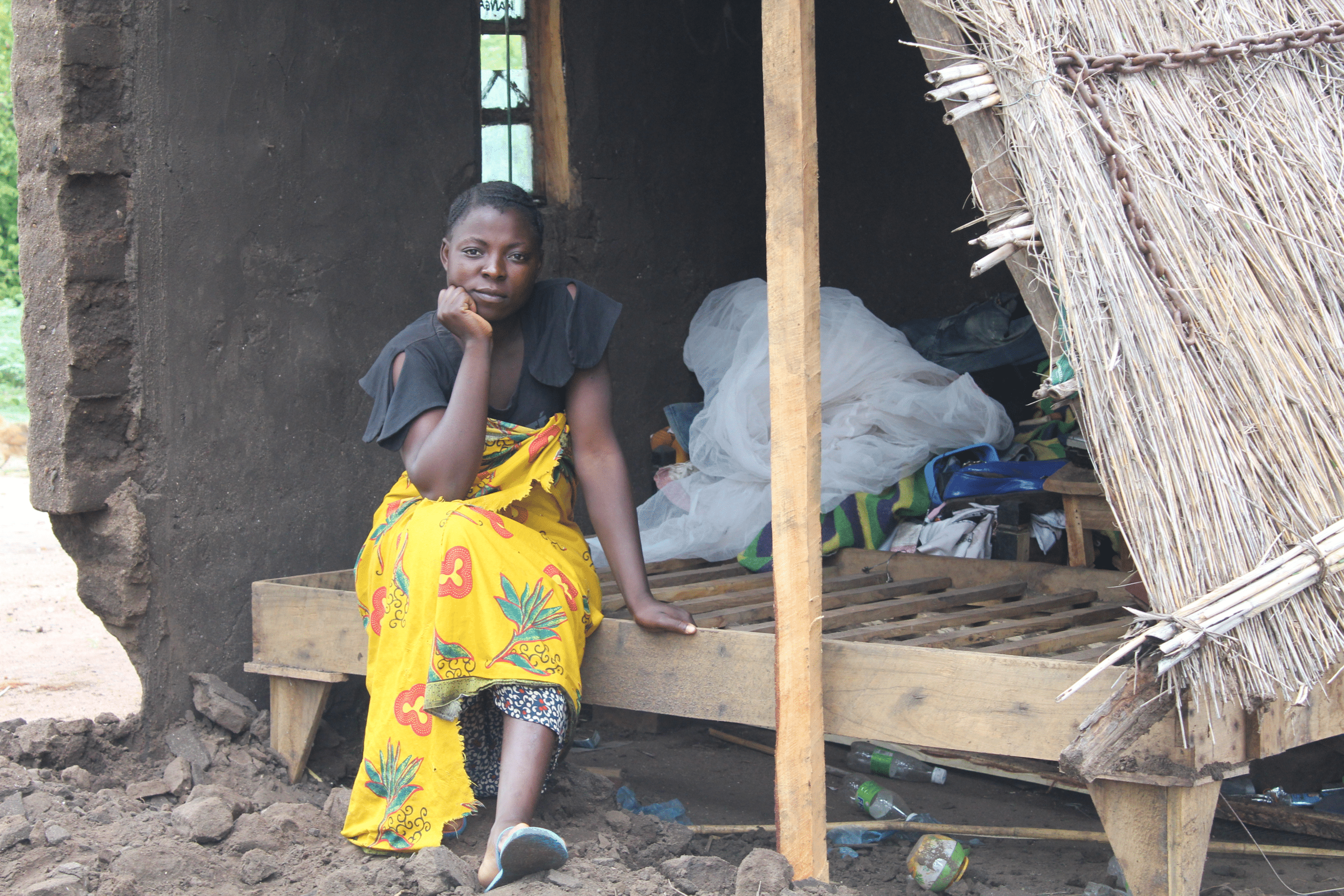 Jenta med kort hår, mørk overdel og gult skjørt sitter i et ødelagt hus i Malawi. Foto: SOS-barnebyer Malawi