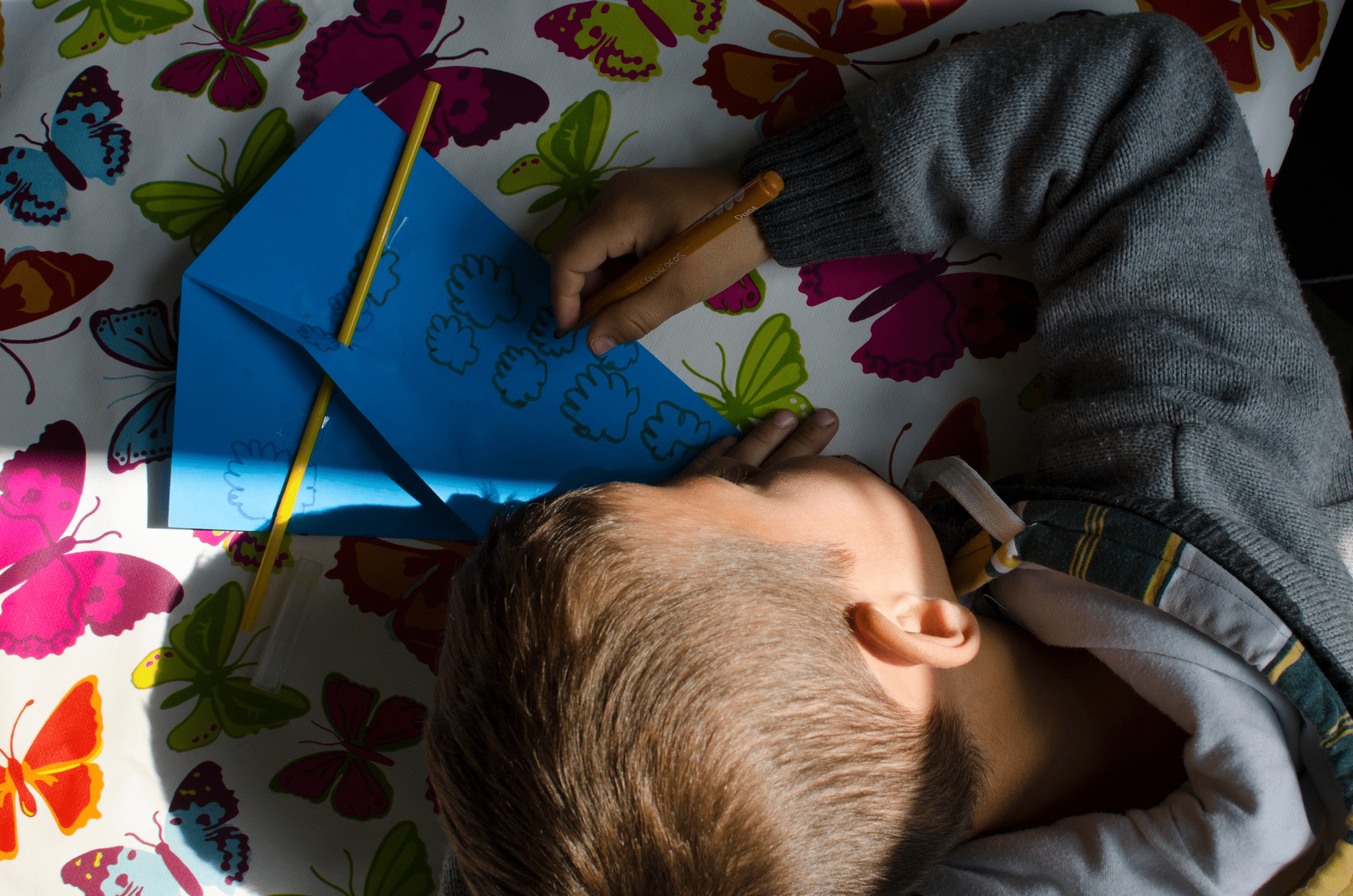 Bilde av en gutt med blondt hår og hettegenser som sitter og tegner på en blå konvolutt. Illustrasjonsbilde: Katerina Ilievska