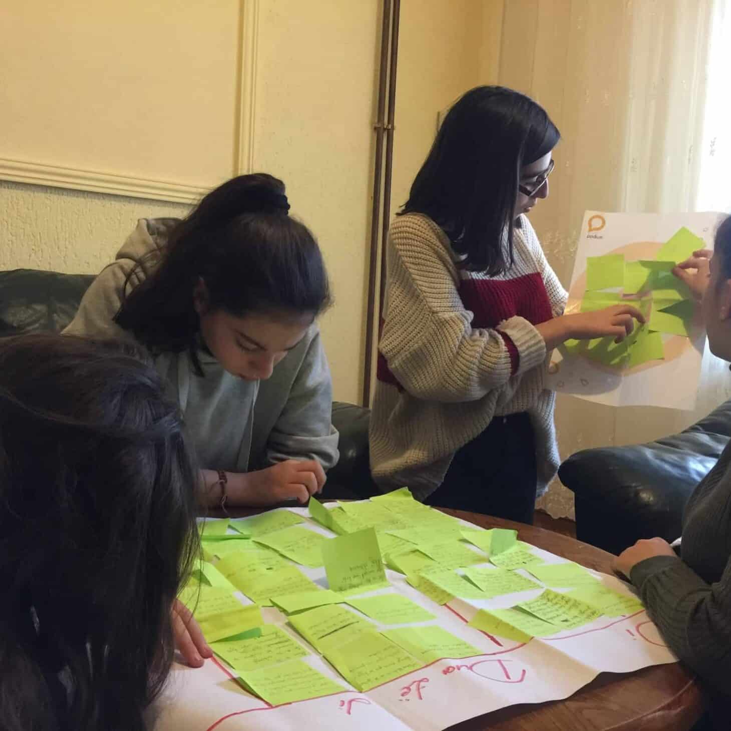 Florina jobber sammen med de andre jentene i nettmobbingprosjektet. På et bord er det et stort hvitt ark med mange grønne post-it lapper. Foto: SOS-barnebyer