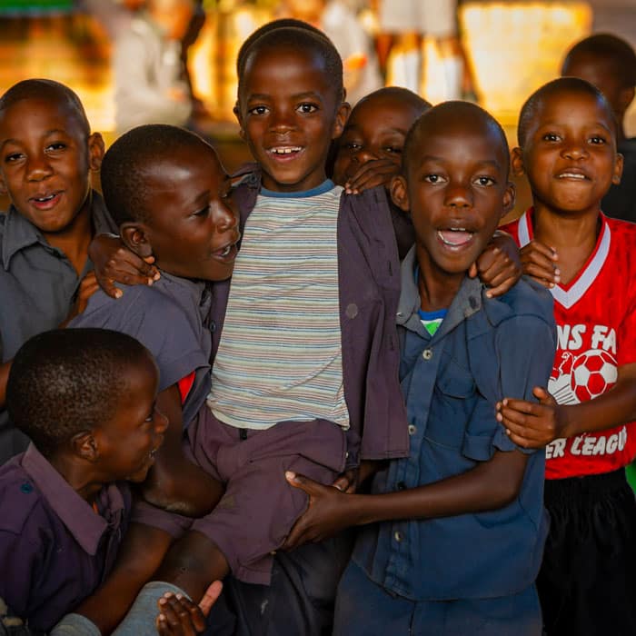 Flere gutter fra Malawi står samlet og smiler. Tre av guttene løfter en annen gutt. Flere av dem har blå skoleuniformer med shorts og skjorte, en har rød fotballgenser. Foto: Cornel van Heerden