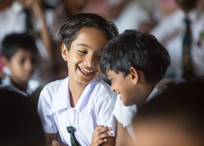 To jenter fra Sri Lanka med kort mørkt år, skoleuniform, hvit skjorte og grønt slips, ser på hverandre og smiler. Foto: Alf Berg
