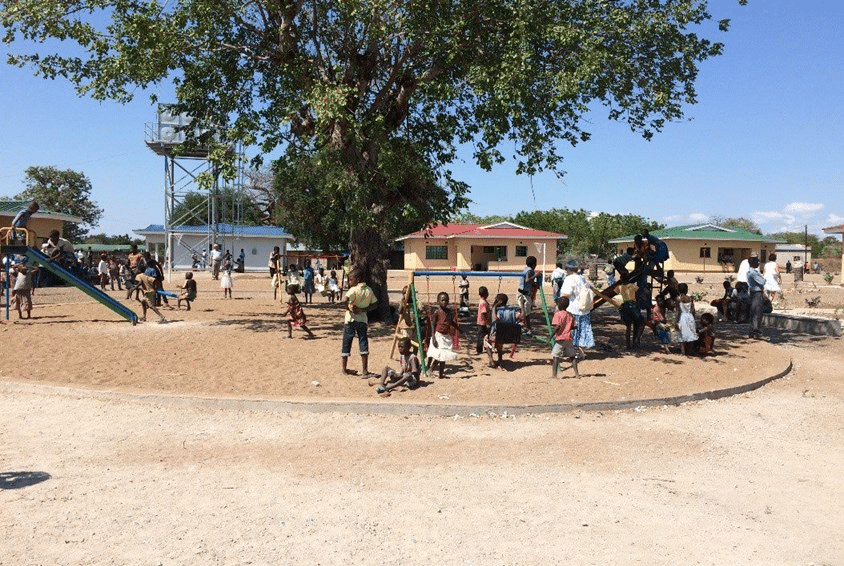 Mange barn leker på lekeplassen. Husene i barnebyer er i bakgrunnen på bildet. Foto: SOS-barnebyer