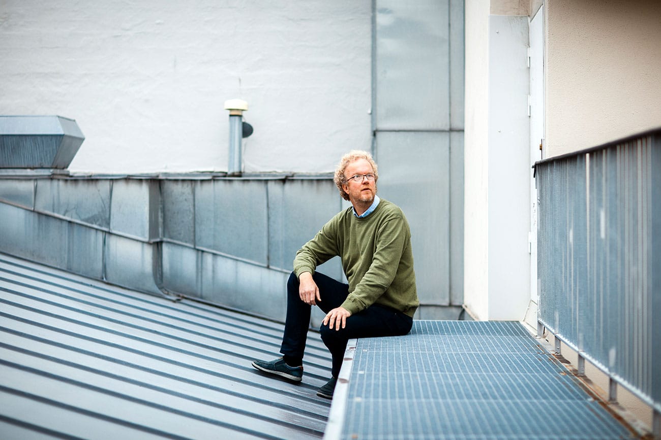 Lasse Kristiansen, Fagforbundet, sitter på et tak. Han har mørk bukse, lyseblå skjorte, grønn genser, krøllete lyst hår, skjegg og briller. Foto Oda Hveem