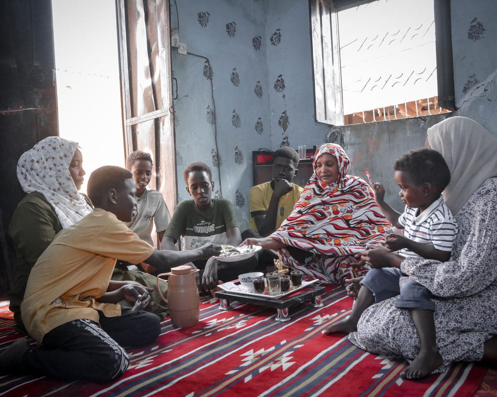 Malik sitter sammen med SOS-fosterfamilien sin på gulvet og spiser. Foto: Ali Abdallah Al