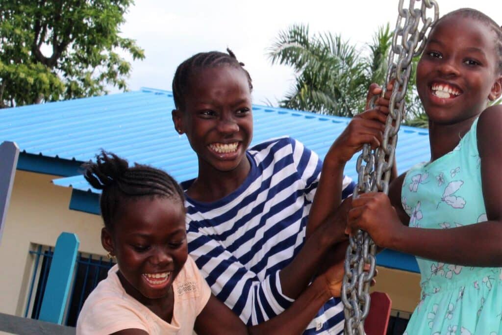 Tre barn Malawi leker og smiler ute i lekeplassen.