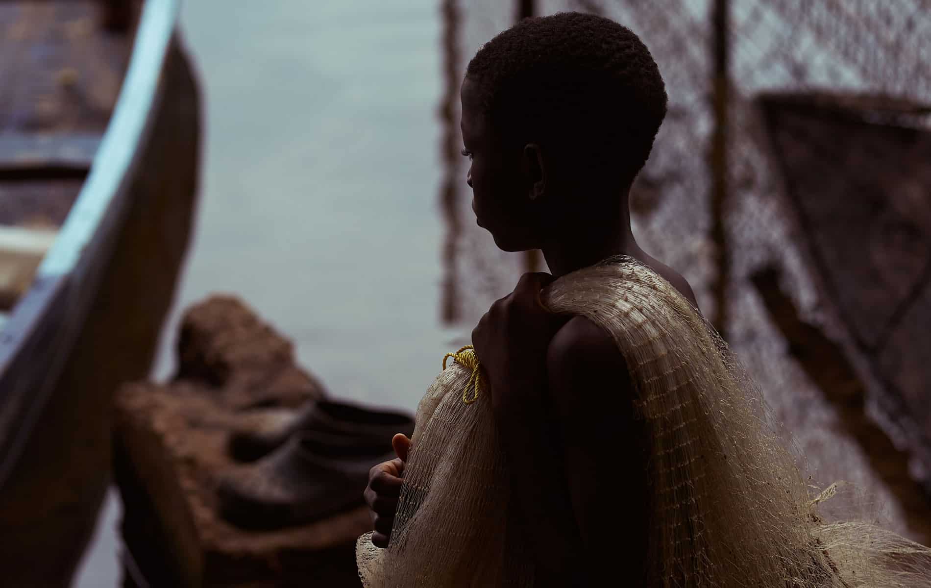 En gutt står på en brygge ved Lake Volta, over skulderen har han et fiskegarn. Foto: Henry KD