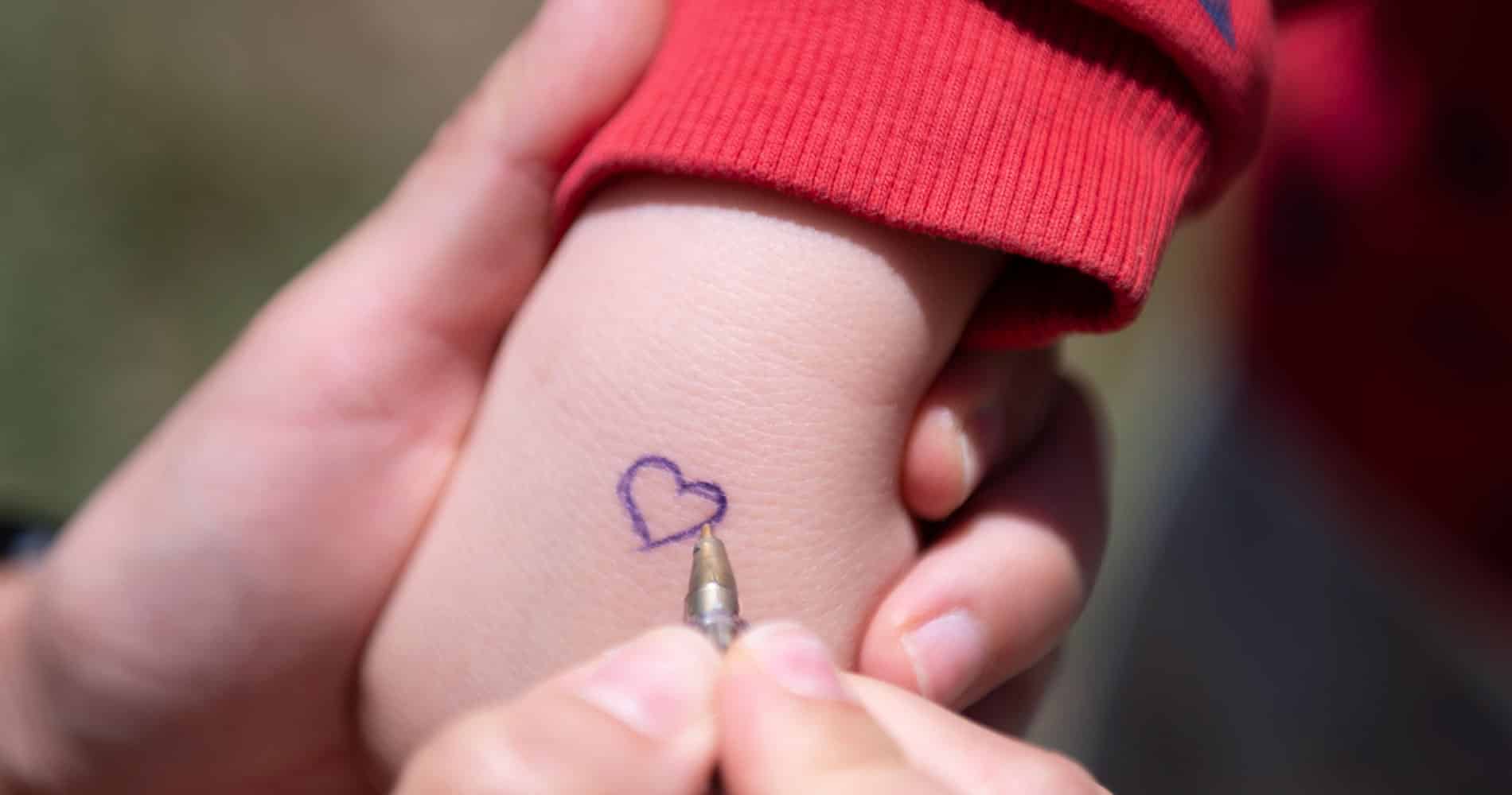 En voksen hånd holder en barnehånd og tegner et hjerte på håndbaken. Foto: Katerina Ilievska