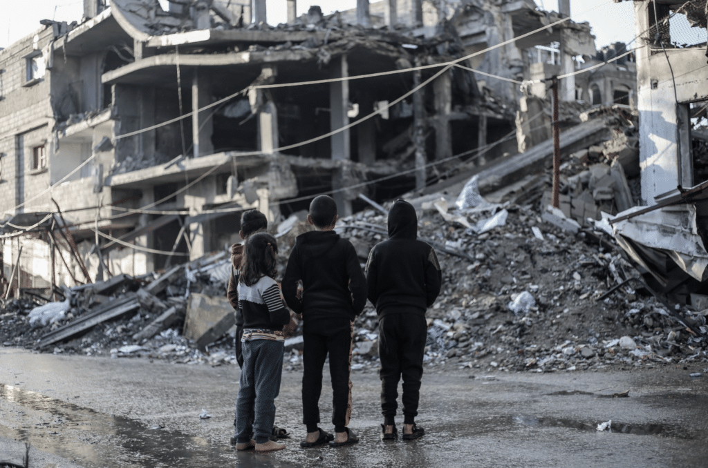 Fire barn i Gaza som står forran ruiner etter bomber. i mørke klær. Mars 2024.