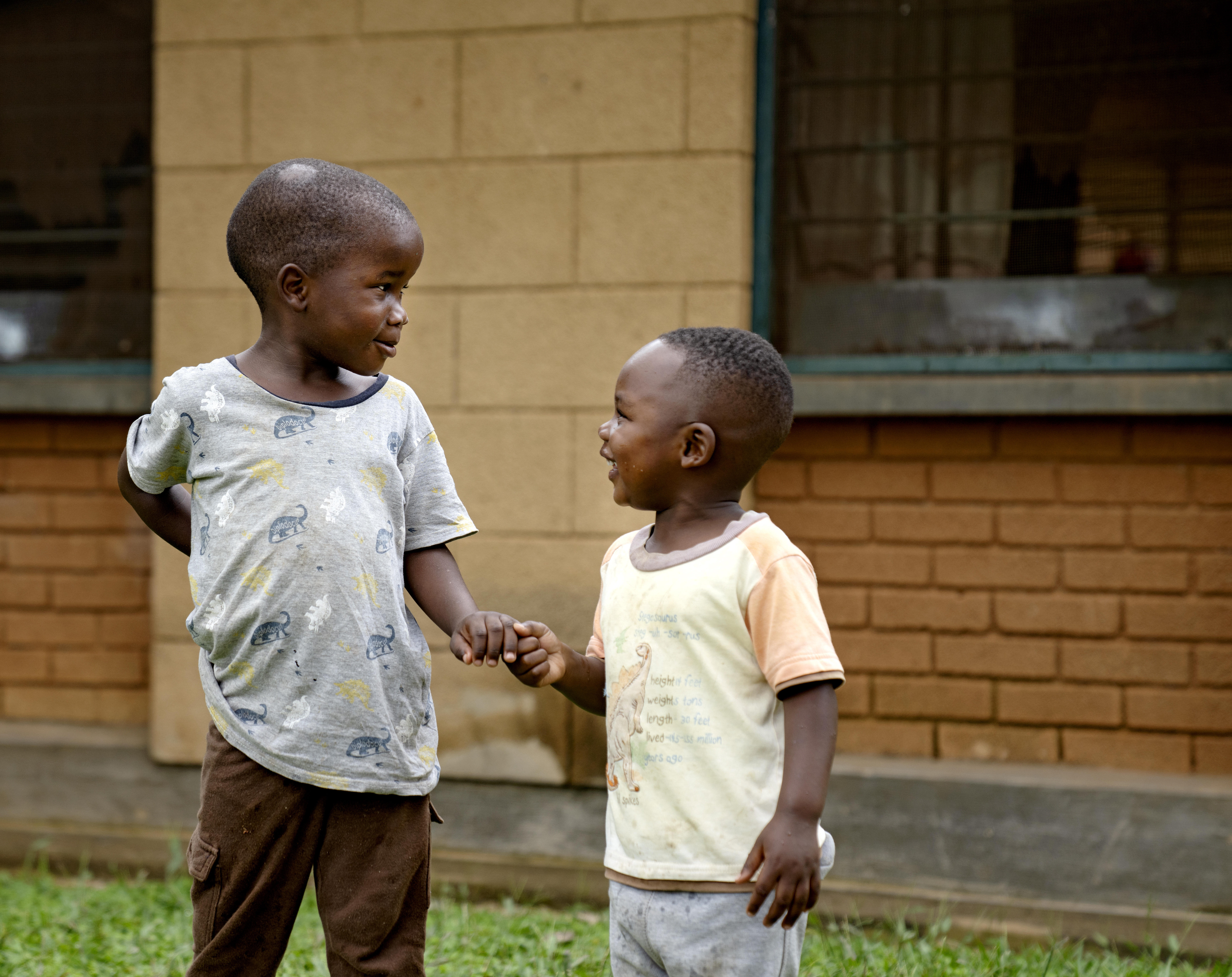 To SOS-brødre i Kakiri, Uganda, som holder hender og smiler til hverandre. Kledd i t-skjorte og bukser.