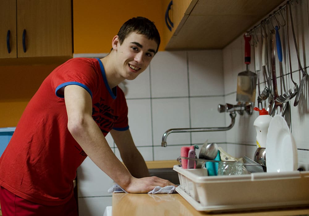 Ung gutt med mørkt, kort hår og rød t-skjorte som smiler, tørker en kjøkkenbenk med en klut. Foto: Katerina Ilievska