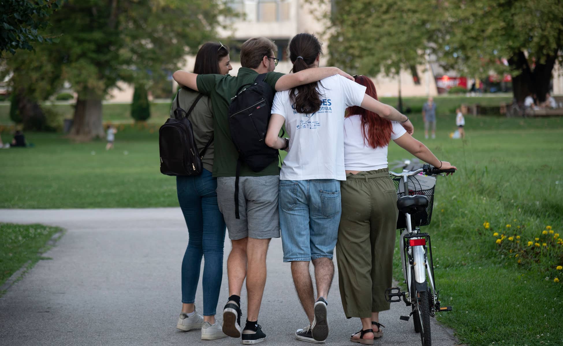 To unge jenter og to unge gutter går på en vei i en park. De holder hverandre rundt skulderen, den ene triller en sykkel. Bildet er tatt bakfra. Foto: Katerina Ilievska