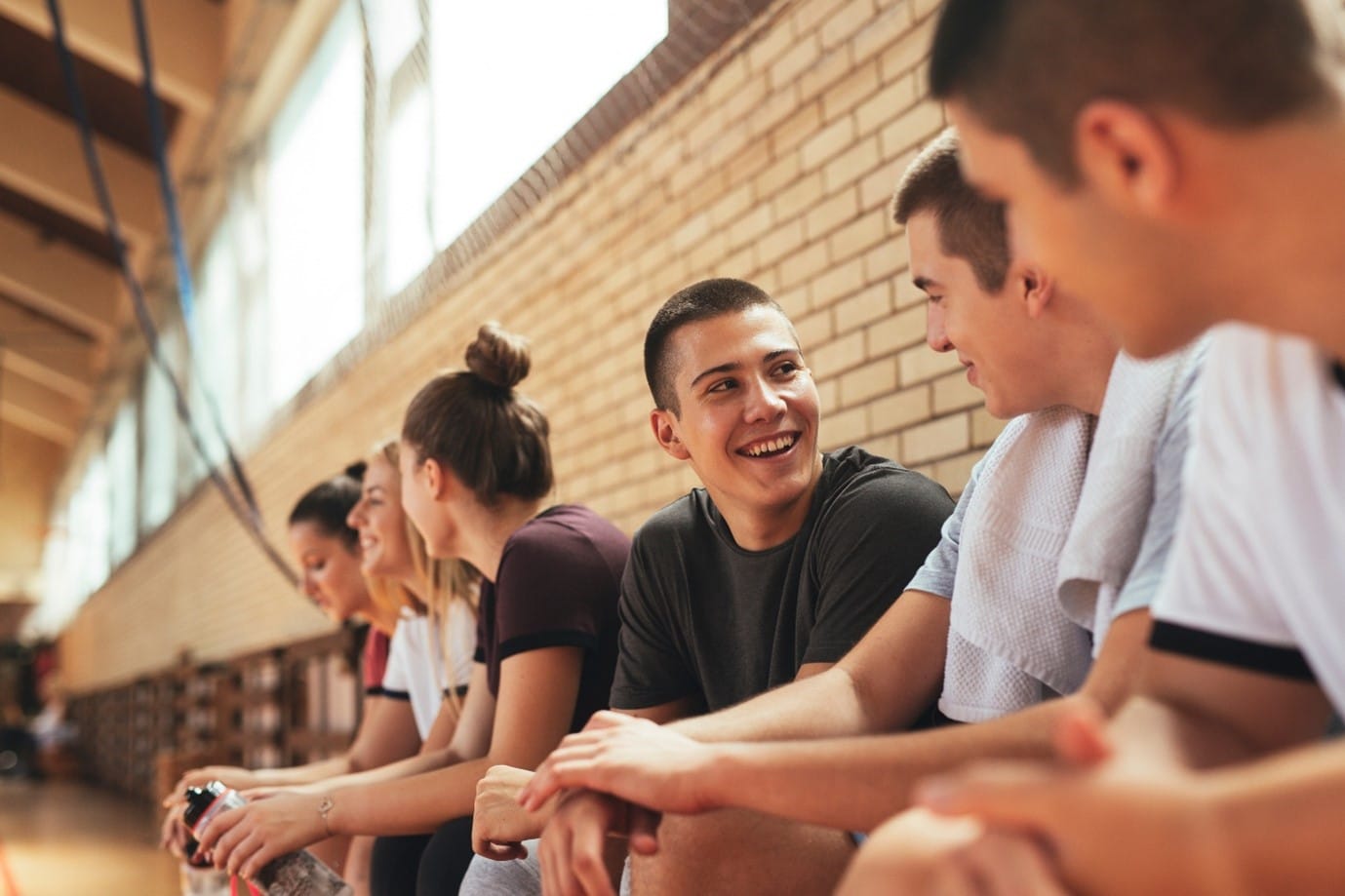 En gruppe ungdommer sitter samlet i en gymsal, men se prater og smiler til hverandre.