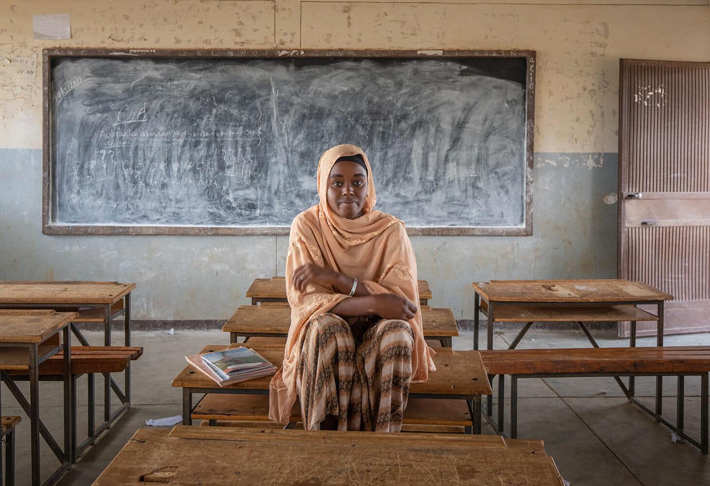 Zala, med ferskenfarget hijab, og rutete kjole sitter på pulten i klasserommet. Foto: Petterik Wiggers