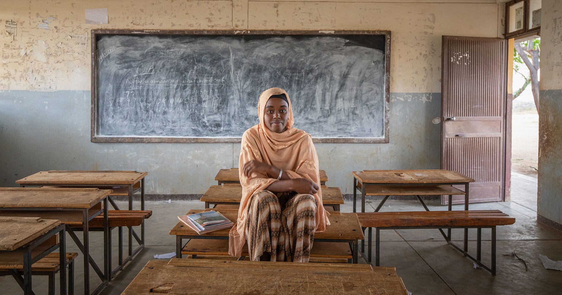 Zala, med ferskenfarget hijab, og rutete kjole sitter på pulten i klasserommet. Foto: Petterik Wiggers