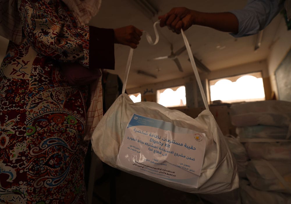 En kvinne med mønstrete kjole tar i mot en bag med hygieneartikler. Foto Mohammad Al Baba