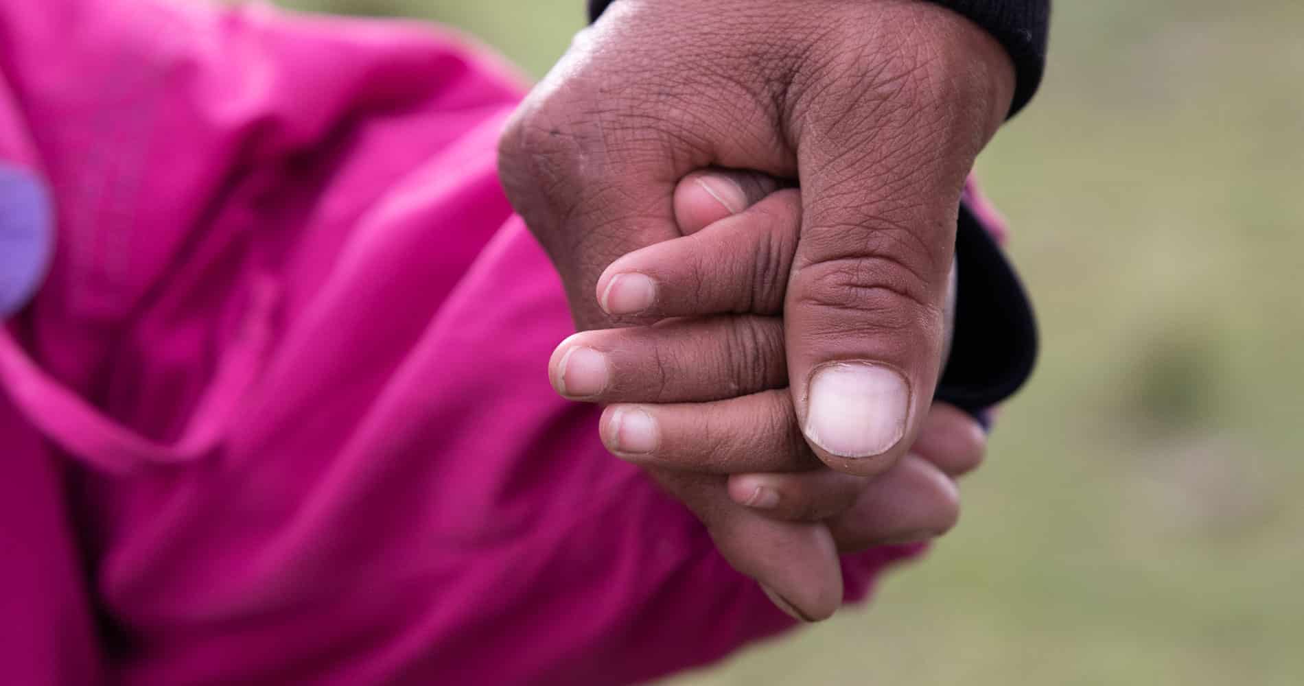 Peru: Bilde av to hender, en far holder datterens hånd, hun har rosa jakke. foto Pierre Devé