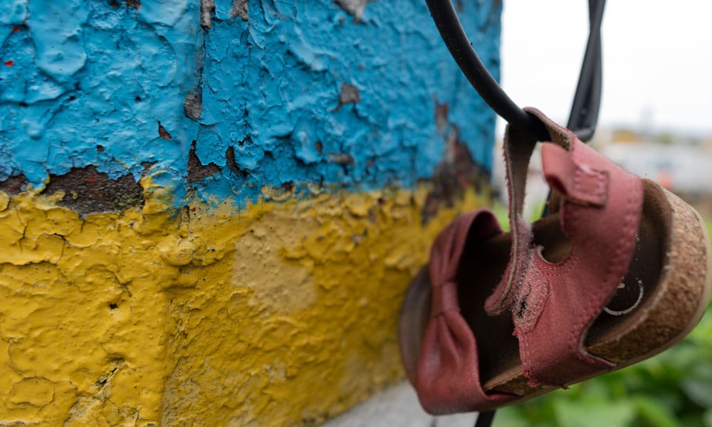 En murvegg malt i det ukrainske flaggets farger, på en ledning henger en liten, rosa, barnesandal. Foto Katerina Ilievska