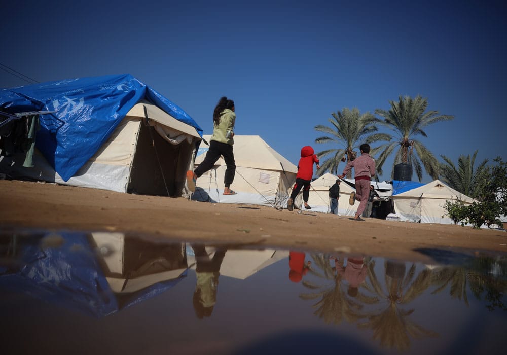 Tre barn løper foran en rekke telt i en av SOS-barnebyers teltleire i Gaza. Foto Mohammad Al Baba