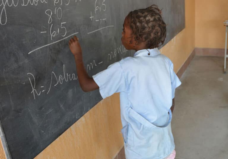 Jente som går på SOS-skolen i Huambo, med lyseblå skoleuniform skriver på tavla. Skolen er en del av SOS-barnebyers arbeid i Huambo som blir støttet av Fagforbundet. Foto Turid Weisser