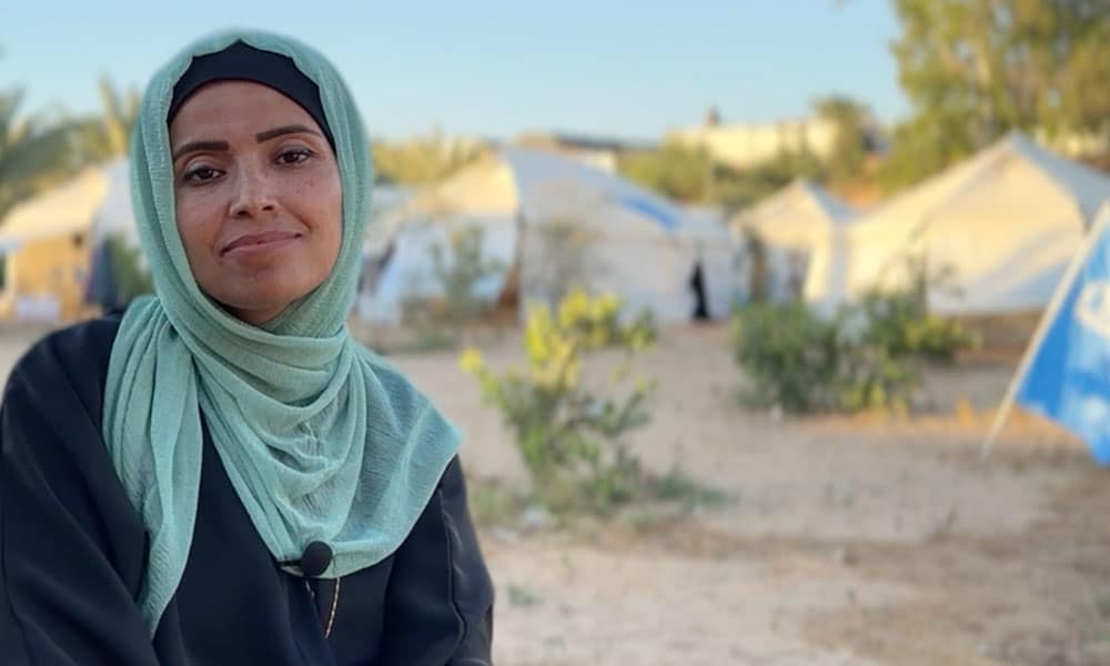 Reem Alreqeb, programsjef for SOS-barnebyene i Gaza. Hun står ute, det er telt i bakgrunnen. Hun har lysegrønn hijab og svart kjole. Foto Mohammad-Al-Bab