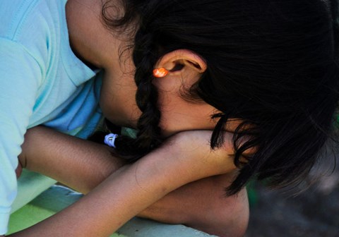 Jente fra Ecuador med mørkt hår i fletter og lyseblå t-skjorte, bøyer seg framover og skjuler ansiktet i hendene. Illustrasjonsfoto: Fernando Espinoza